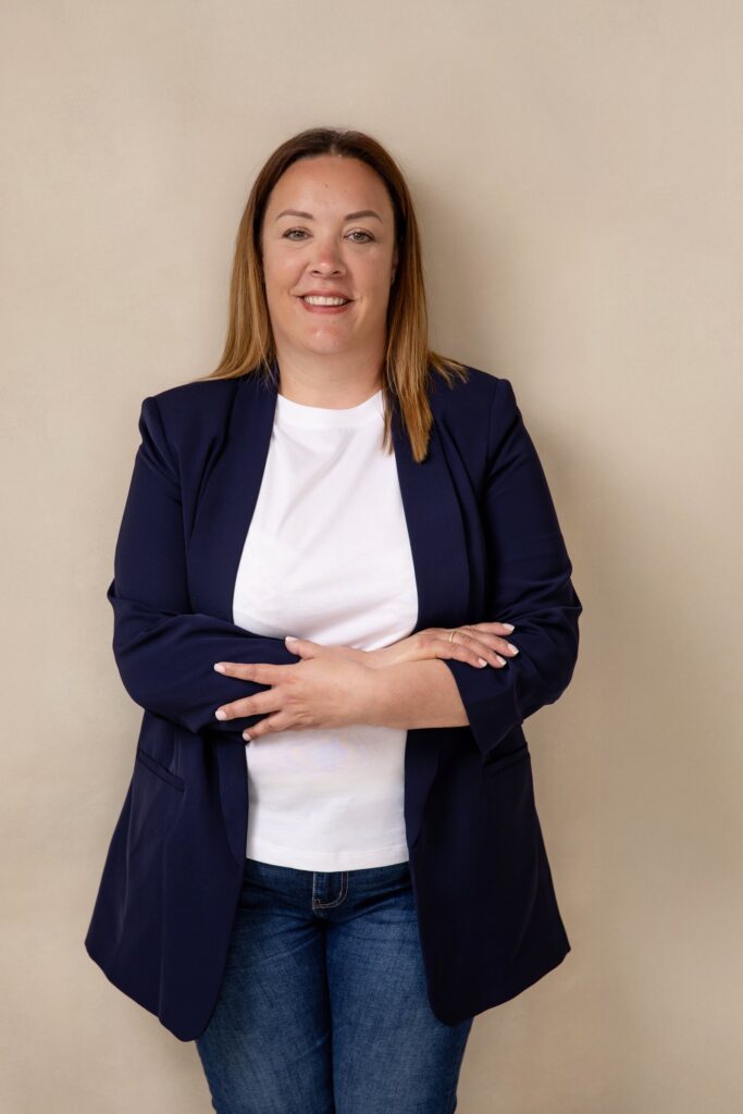 Clair Bryant smiling with her arms folded, in a navy blazer and jeans