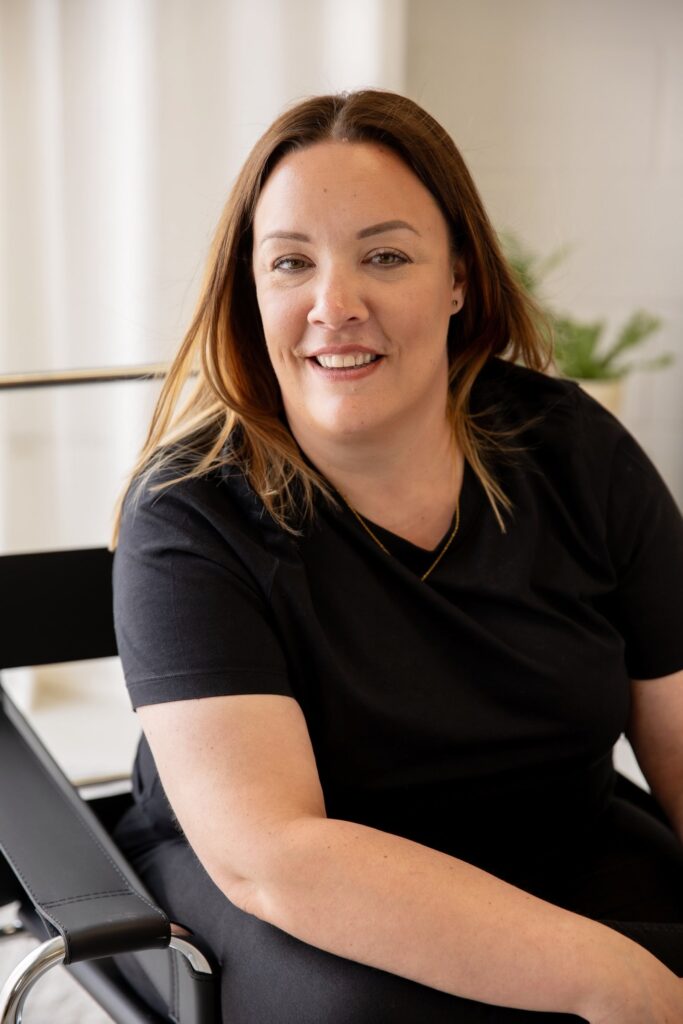Clair Bryant sitting in a black chair and smiling in a bright studio