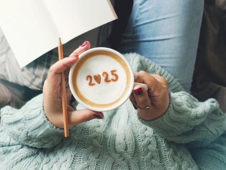 Hands holding a cup of coffee with 2025 drawn in the foam