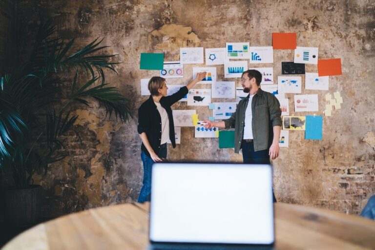 Two colleagues pointing at charts and notes pinned to a wall