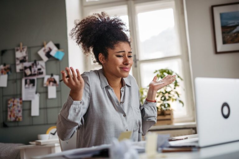 A frustrated woman at her laptop throwing up her hands