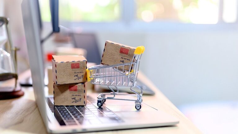 A miniature shopping trolley full of small parcels on a laptop keyboard