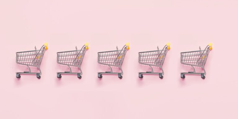 A row of miniature shopping trolleys on a pink background